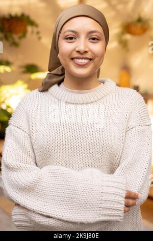 Portrait d'une femme biraciale heureuse portant le hijab, regardant l'appareil photo et souriant Banque D'Images