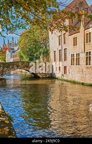 Des maisons bordent le canal de Groenerei à Bruges, en Belgique, avec des arbres d'automne sous un ciel bliue. Banque D'Images