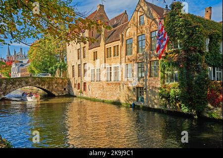 Des maisons bordent le canal de Groenerei à Bruges, en Belgique, avec des arbres d'automne sous un ciel bliue. Banque D'Images