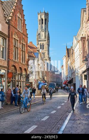 Pédaler le long des rues pavées du centre de Bruges, avec le beffroi de Bruges en arrière-plan Banque D'Images