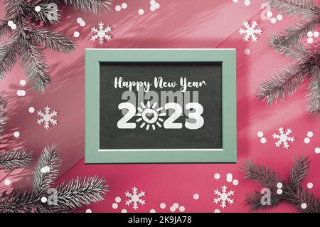 Bonne année 2023, soleil avec coeur dessin animé à la place de zéro chiffre. Arrière-plan d'hiver simple. Branches de sapin sur papier rose bicolore avec confetti Banque D'Images