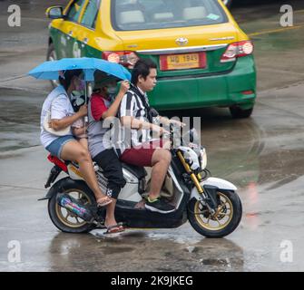 SAMUT PRAKAN, THAÏLANDE, OCT 04 2022, Un homme conduit deux femmes cachées sous un parapluie sur une moto Banque D'Images