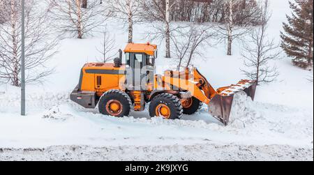 Déneigement. Le tracteur se dégage après de fortes chutes de neige. Un gros tracteur orange élimine la neige de la route et dégage le trottoir. Nettoyage des routes Banque D'Images