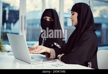 Deux jeunes femmes d'affaires arabes travaillant sur un ordinateur portable dans leur bureau. Banque D'Images