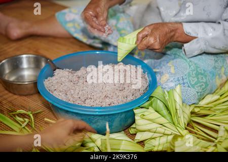 Mains de la femme âgée enveloppant le riz collant avec des feuilles de palmier ou Ketopas Palas Banque D'Images