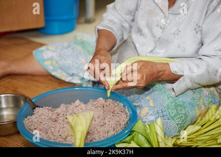Mains de la femme âgée enveloppant le riz collant avec des feuilles de palmier ou Ketopas Palas Banque D'Images