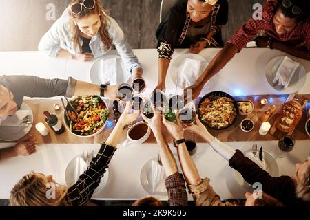 Des encouragements à l'amitié et à la bonne nourriture. Un groupe de jeunes amis qui font un toast lors d'un dîner. Banque D'Images