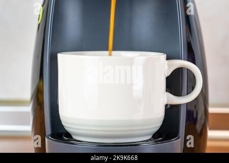 Tasse de pocélain blanc dans une cafetière automatique pendant que le café sort fraîchement préparé. Banque D'Images