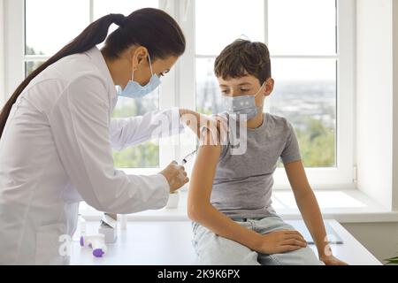 Une femme médecin effectue une injection de vaccin antiviral pour un garçon préadolescent dans un centre de vaccination. Banque D'Images