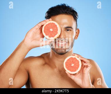 Beauté, pamplemousse et soin de la peau avec un modèle homme en studio sur fond bleu pour promouvoir le traitement naturel. Nourriture, bien-être et portrait avec un Banque D'Images