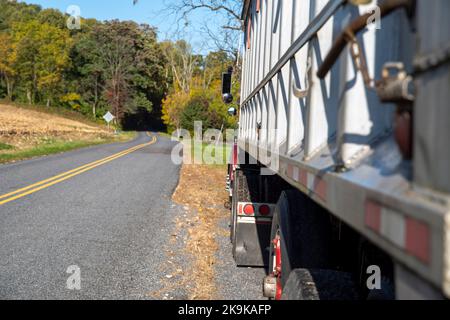 Vue latérale du camion de ferme garé sur une route de campagne avec des champs de feuillage d'automne Banque D'Images