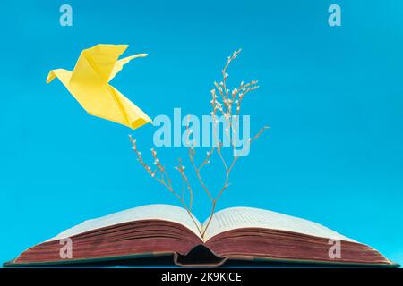 L'origami jaune vole depuis un vieux livre sur fond bleu. Gros plan sur un arbre sec issu d'un livre Banque D'Images