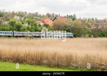 Un vieux train électrique traverse la région peuplée de ​​Petrovaradin, Novi Sad, Serbie. Banque D'Images