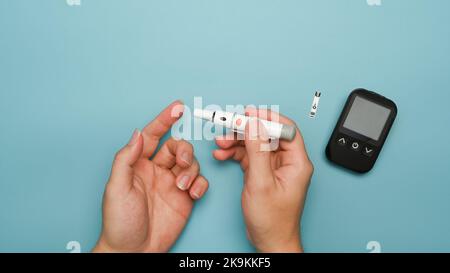 Au-dessus de la vue de l'homme diabétique prenant un échantillon de sang lancet stylo sur fond bleu. Diabète et concept de soins de santé Banque D'Images