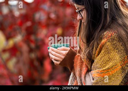 Mains tenant vert mug automne thé humeur rouge oliage flou bokeh arrière-plan extérieur matin boire automne confortable concept, couverture de vacances rétro-éclairée Banque D'Images