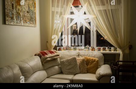 Maison confortable, décorations de Noël: Étoiles lumineuses, beaucoup de maisons colorées sur le seuil de la fenêtre, oreillers doux. Banque D'Images