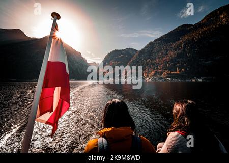 Vue d'automne pittoresque du village de montagne Hallstatt, Salzkammergut, OÖ, Autriche, vue depuis le ferry sur le lac Hallstatt avec drapeau autrichien et touristes Banque D'Images