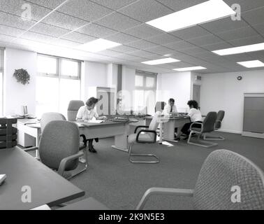 1989, historique, un homme et une femme travaillant à leurs bureaux dans un grand bureau ouvert, Angleterre, Royaume-Uni. Grands bureaux semi-circulaires avec chaises environnantes pour les réunions informelles - dont l'un a lieu - et ordinateurs personnels de l'époque en démonstration. Banque D'Images