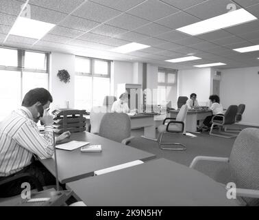 1989, bureau à espace ouvert historique et spacieux, Angleterre, Royaume-Uni, employés de l'entreprise travaillant dans de grands bureaux semi-circulaires, un homme parlant au téléphone, un autre homme ayant une discussion un à un avec une femme membre du personnel. Un ordinateur personnel du jour est assis sur le côté de l'un des bureaux. Banque D'Images