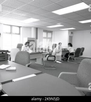 1989, historique, un homme et une femme travaillant à leurs bureaux dans un grand bureau ouvert, Angleterre, Royaume-Uni. Grands bureaux semi-circulaires avec chaises environnantes pour des réunions informelles - dont l'un a lieu - et un ordinateur personnel de l'époque en démonstration. Banque D'Images