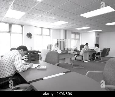 1989, employés historiques, hommes et femmes travaillant à leur bureau dans un grand bureau ouvert, Angleterre, Royaume-Uni. De grands bureaux semi-circulaires avec des chaises environnantes pour des réunions informelles et des ordinateurs personnels de l'époque peuvent être vus. Banque D'Images