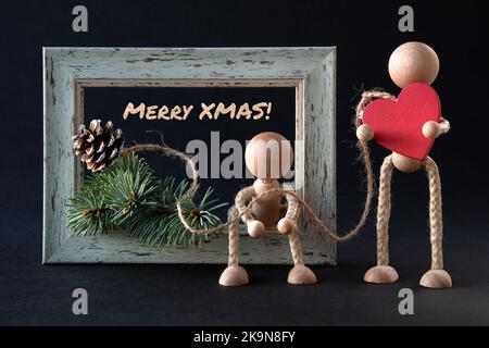 Organisation créative de Noël. Figurines de jeu en bois, hommes par cadre texturé avec branche de sapin et cône de pin. Un homme tient cœur en bois rouge Banque D'Images