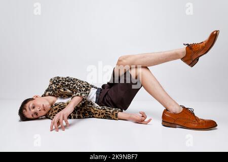 Portrait d'un jeune garçon élégant en veste à imprimé animal et chaussures de rigue classiques posé isolé sur fond gris. Haute couture Banque D'Images