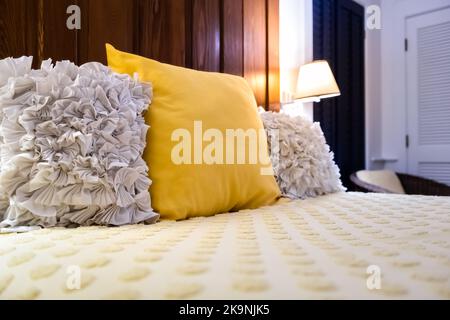 Coussin décoratif jaune et blanc en mousseline rose sur le lit de la chambre avec couette en duvet douce le soir avec lampe de chevet éclairée Banque D'Images