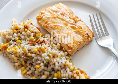Macro gros plan de mahi mahi poisson fruits de mer cuit filet sur plaque blanche avec fourchette en mélange de pâtes couscous orzo, fente bébé garbanzos et le quinoa rouge Banque D'Images