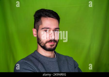 Jeune homme avec des vêtements décontractés, exprimant des émotions, posant sur fond vert Banque D'Images