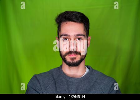 Jeune homme avec des vêtements décontractés, exprimant des émotions, posant sur fond vert Banque D'Images