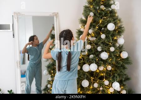 Petite fille d'enfant est la décoration de l'arbre de Noël à l'intérieur. Le matin avant Noël Banque D'Images