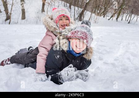 Les enfants heureux en hiver rient en jouant dans la chasse à la neige à l'extérieur. Vacances d'hiver pour les enfants Banque D'Images