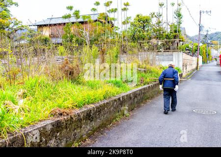 Kyoto, Japon - 11 avril 2019: Homme âgé senior marchant avec bâton de bois derrière l'exercice dans le quartier résidentiel avec des maisons et le jardin Banque D'Images