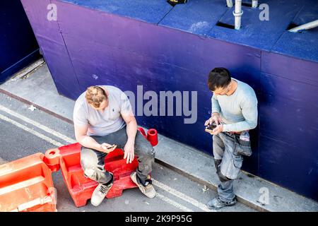 Londres, Royaume-Uni - 22 juin 2018: Deux ouvriers de la construction hommes prenant la pause déjeuner, utilisant des téléphones à l'extérieur de la rue de la ville de Westminster Banque D'Images