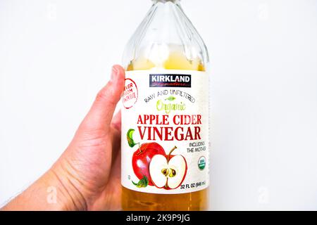 Naples, Etats-Unis - 21 octobre 2021: Macro-gros plan de la main tenant le vinaigre de cidre de pomme biologique non filtré brut par la marque Costco Kirkland Banque D'Images