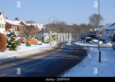 Une rue urbaine résidentielle courbée après la chute de neige, avec la neige sur la surface de la route se tournant vers la neige fondante et les ordures dehors pour la collecte Banque D'Images