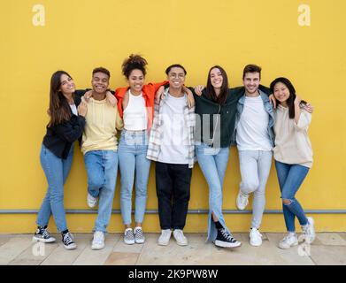 Groupe de jeunes amis multiethniques riant en regardant la caméra sur un mur jaune. Amitié et diversité Banque D'Images