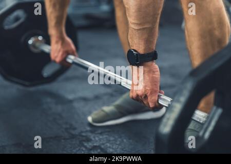 Gros plan montrant seulement les mains et les jambes d'un homme caucasien musclé fort non reconnu se préparer à soulever une barbell. Accessoires de gym : montre. . Photo de haute qualité Banque D'Images