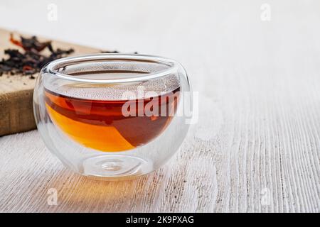 Tasse en verre avec thé noir aromatique sur table en bois blanc Banque D'Images