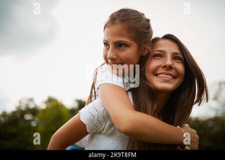 Les sœurs sont là pour se soutenir les unes les autres. Une jeune fille qui donne à sa jeune sœur une promenade de pigeyback à l'extérieur. Banque D'Images