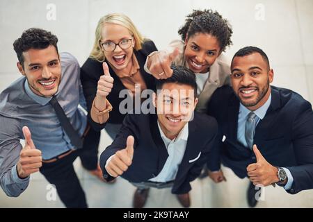 Un groupe de collègues de travail animés. Portrait en grand angle d'un groupe de jeunes hommes d'affaires joyeux montrant les pouces dans les airs tout en restant debout Banque D'Images