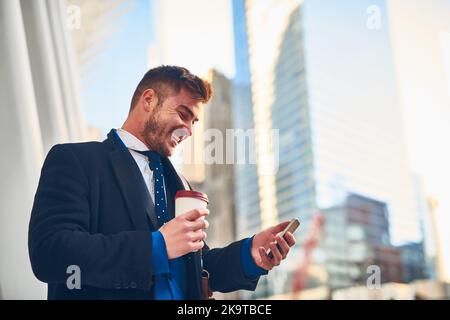 Regardez ce qui mister populaire aujourd'hui. Un jeune homme joyeux textant sur son téléphone tout en buvant du café au travail pendant les heures du matin. Banque D'Images