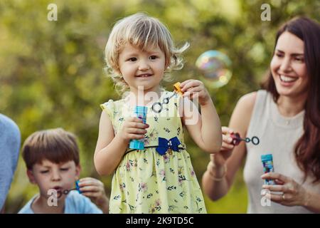 Dehors pour un peu de bulle de plaisir. Une adorable petite fille soufflant des bulles avec sa famille dehors. Banque D'Images