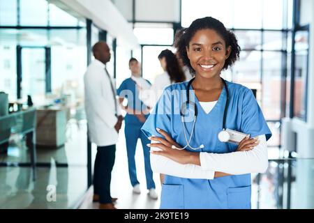 J'aime voir mes patients bien. Portrait d'un jeune médecin confiant travaillant dans un hôpital avec ses collègues en arrière-plan. Banque D'Images