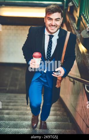 Monter les escaliers de la réussite. Portrait d'un jeune homme d'affaires gai envoyant un message texte au téléphone et buvant un café tout en marchant dans un escalier Banque D'Images