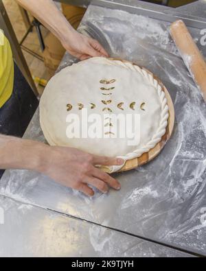 Les mains fermant la tarte ossète farcie de viande hachée sur la table métallique de la cuisine du restaurant. Banque D'Images