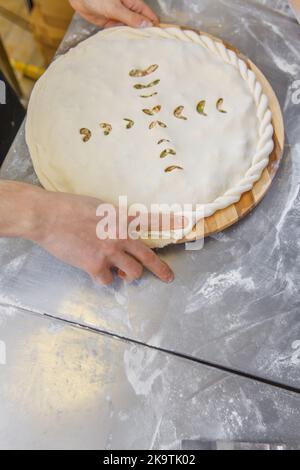 Les mains fermant la tarte ossète farcie de viande hachée sur la table métallique de la cuisine du restaurant. Banque D'Images