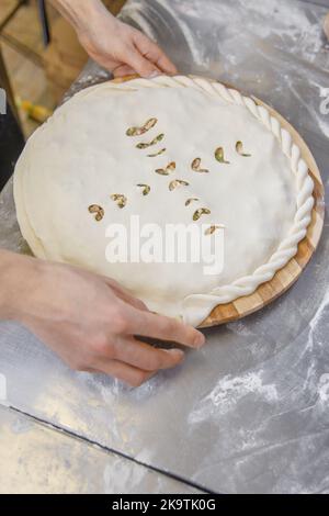 Les mains fermant la tarte ossète farcie de viande hachée sur la table métallique de la cuisine du restaurant. Banque D'Images