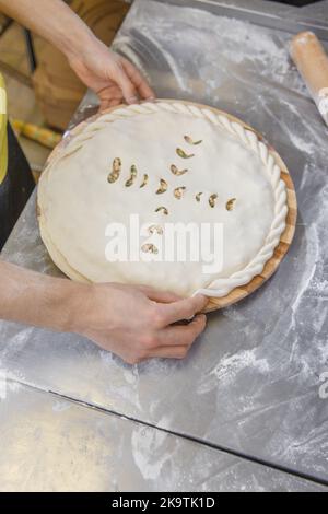 Les mains fermant la tarte ossète farcie de viande hachée sur la table métallique de la cuisine du restaurant. Banque D'Images